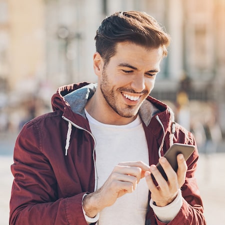 Man with white teeth smiling as he texts his friends on his phone