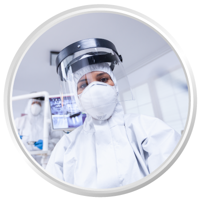 Dental professional in full protective gear, including a mask and face shield, ensuring safety during patient care in a dental office setting.
