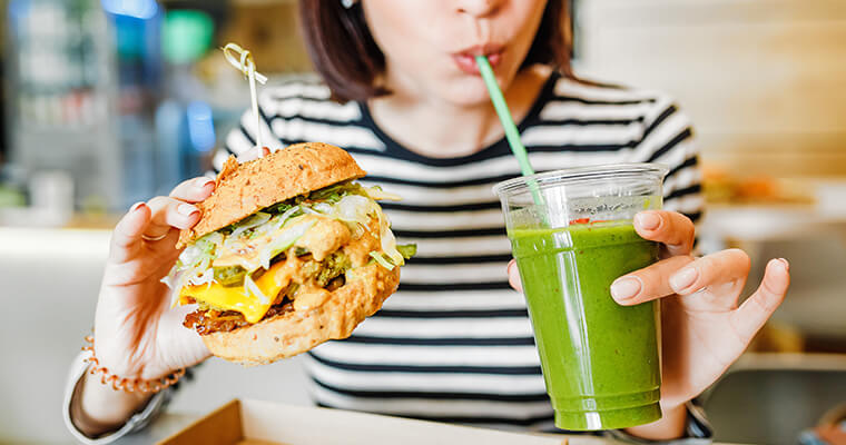 woman holding a burger and drinking through a straw